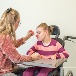 a woman spoon-feeding young kid in a wheelchair